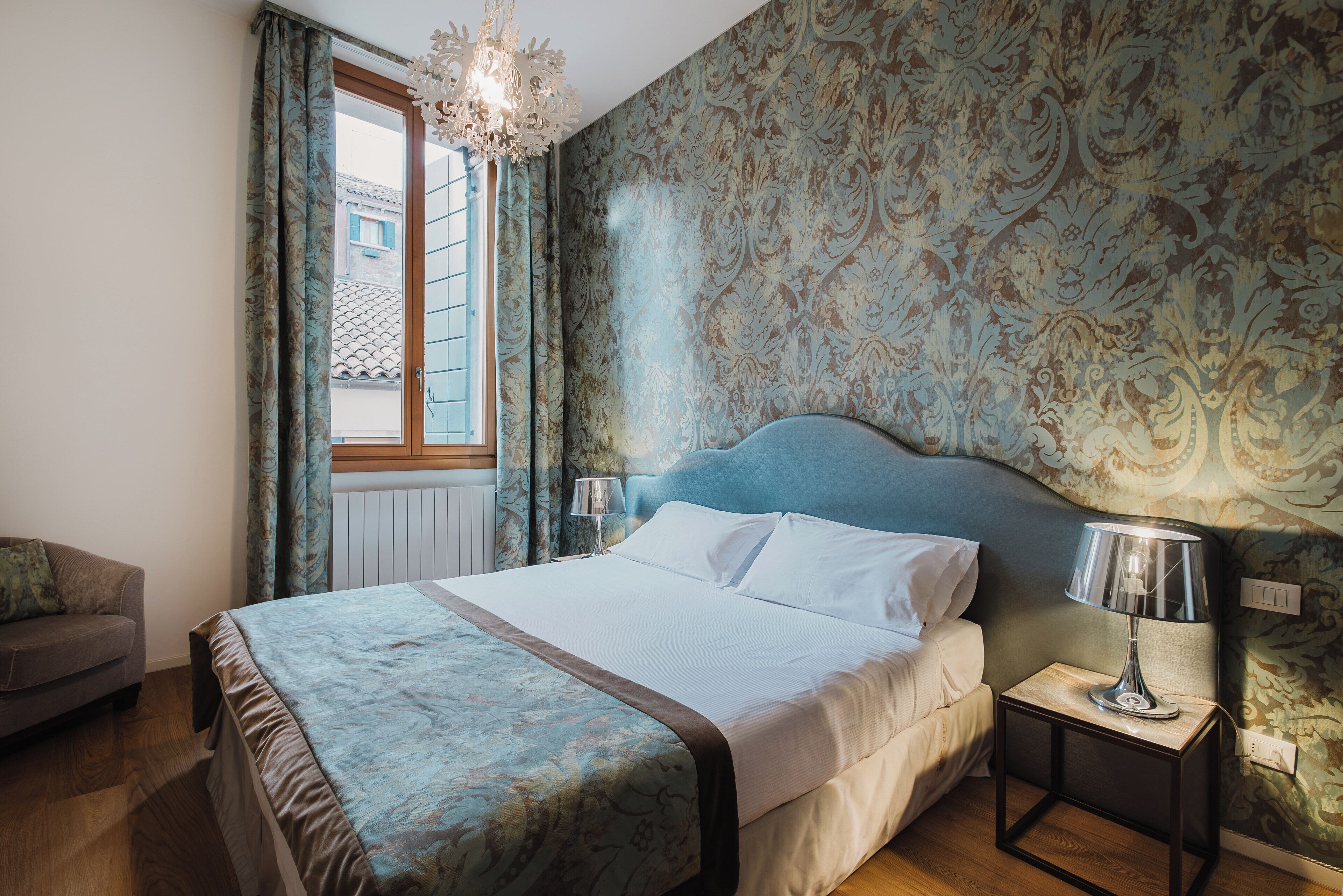 A bedroom with a large bed, a nightstand with a lamp, a dresser, and a window with curtains.