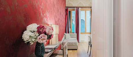 Un pasillo con pared roja, una silla blanca, una mesita con un florero y suelo de madera.