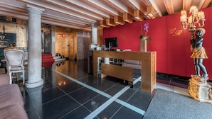 En hotellobby med en receptionsdisk, en staty och en röd vägg med initialerna ”LR”.