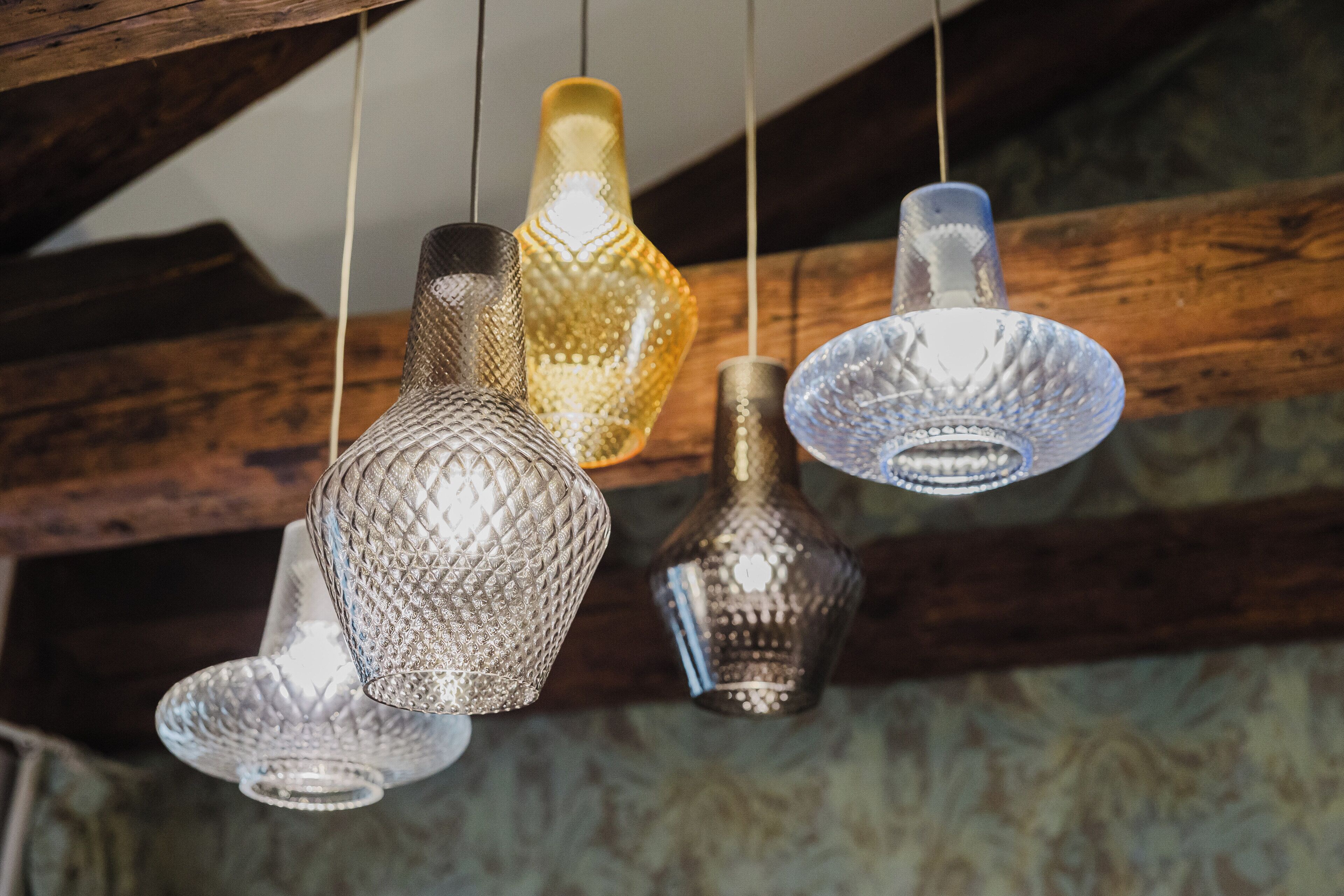 A ceiling with wooden beams and hanging glass lamps with textured designs.
