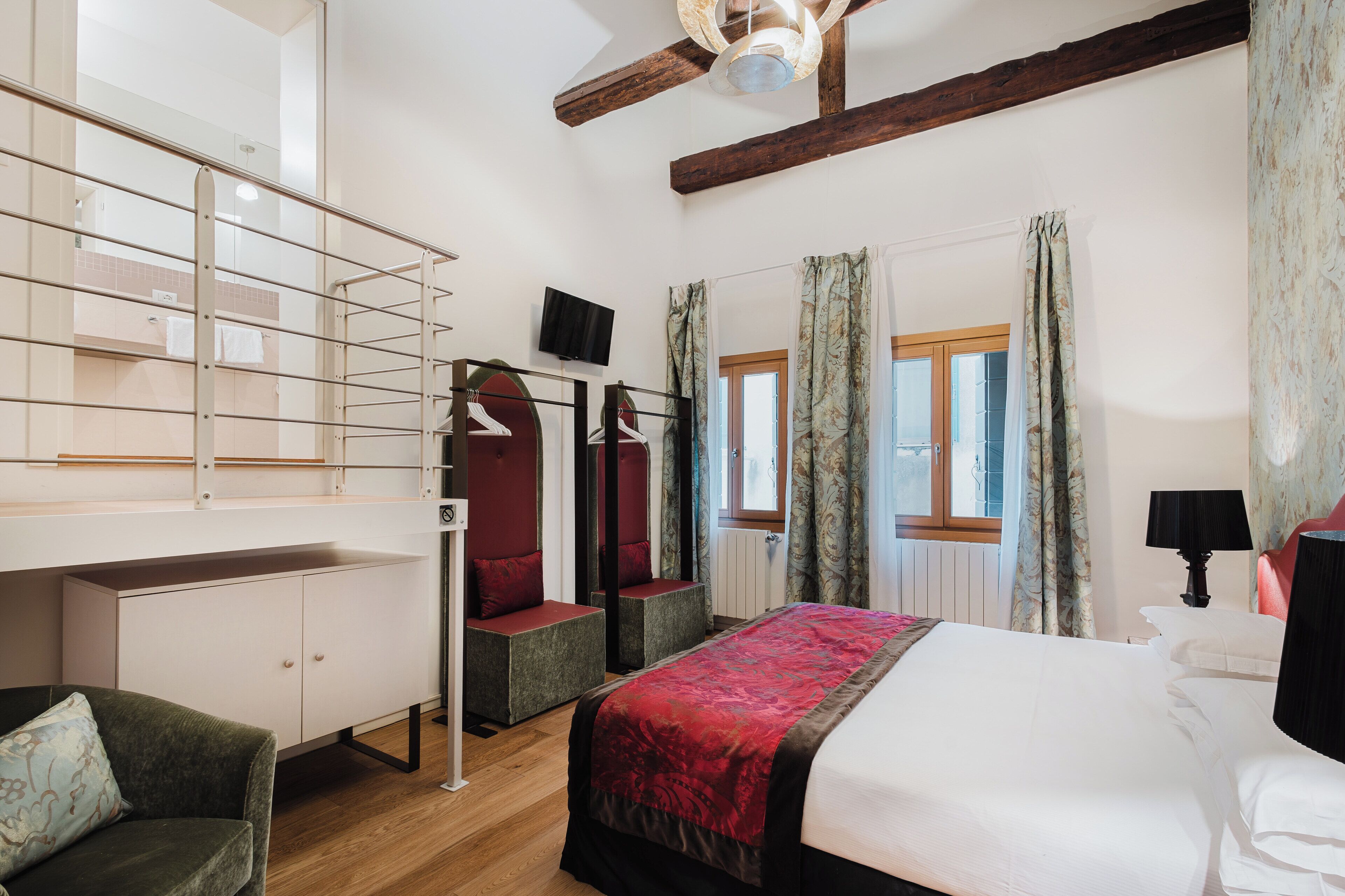 A hotel room with a bed, a desk with a chair, a wardrobe, and a mirror.