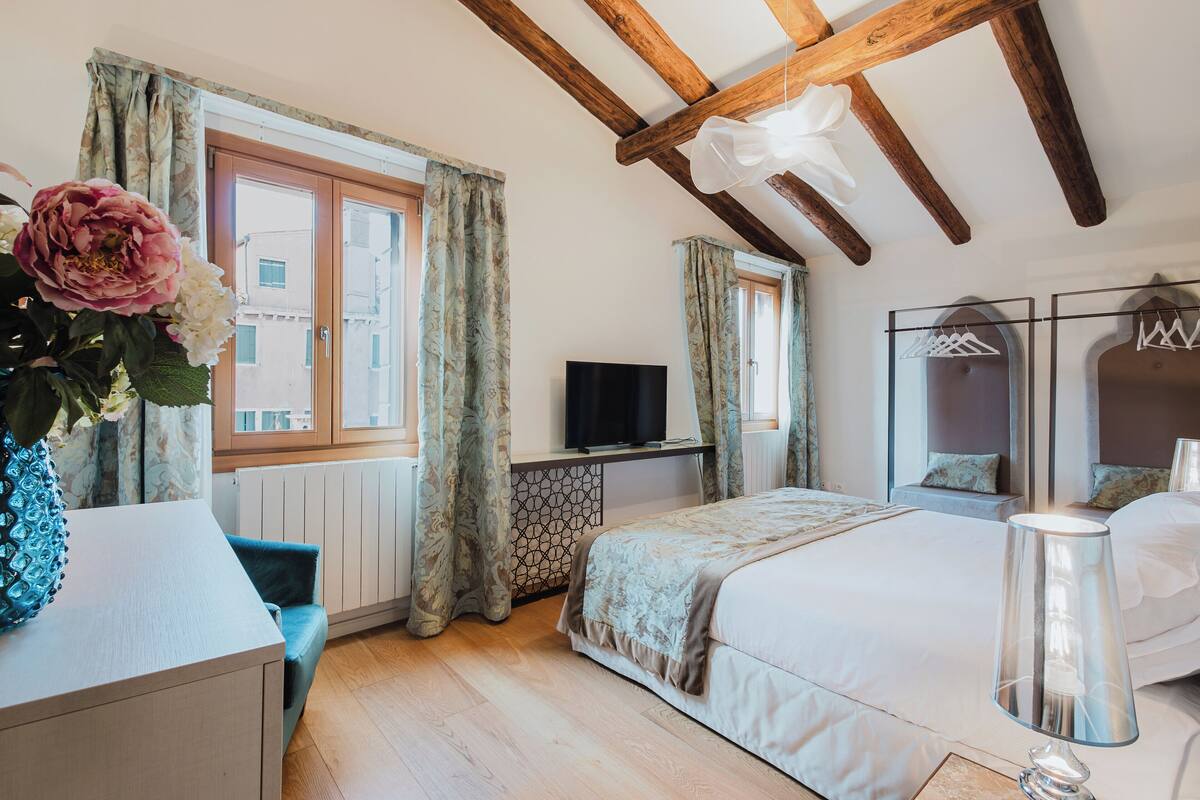 Una camera da letto con un letto, una TV, una cassettiera, una sedia e una finestra con tende.