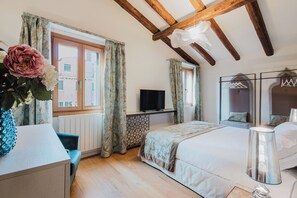 Een slaapkamer met een bed, een televisie, een dressoir, een stoel en een raam met gordijnen.