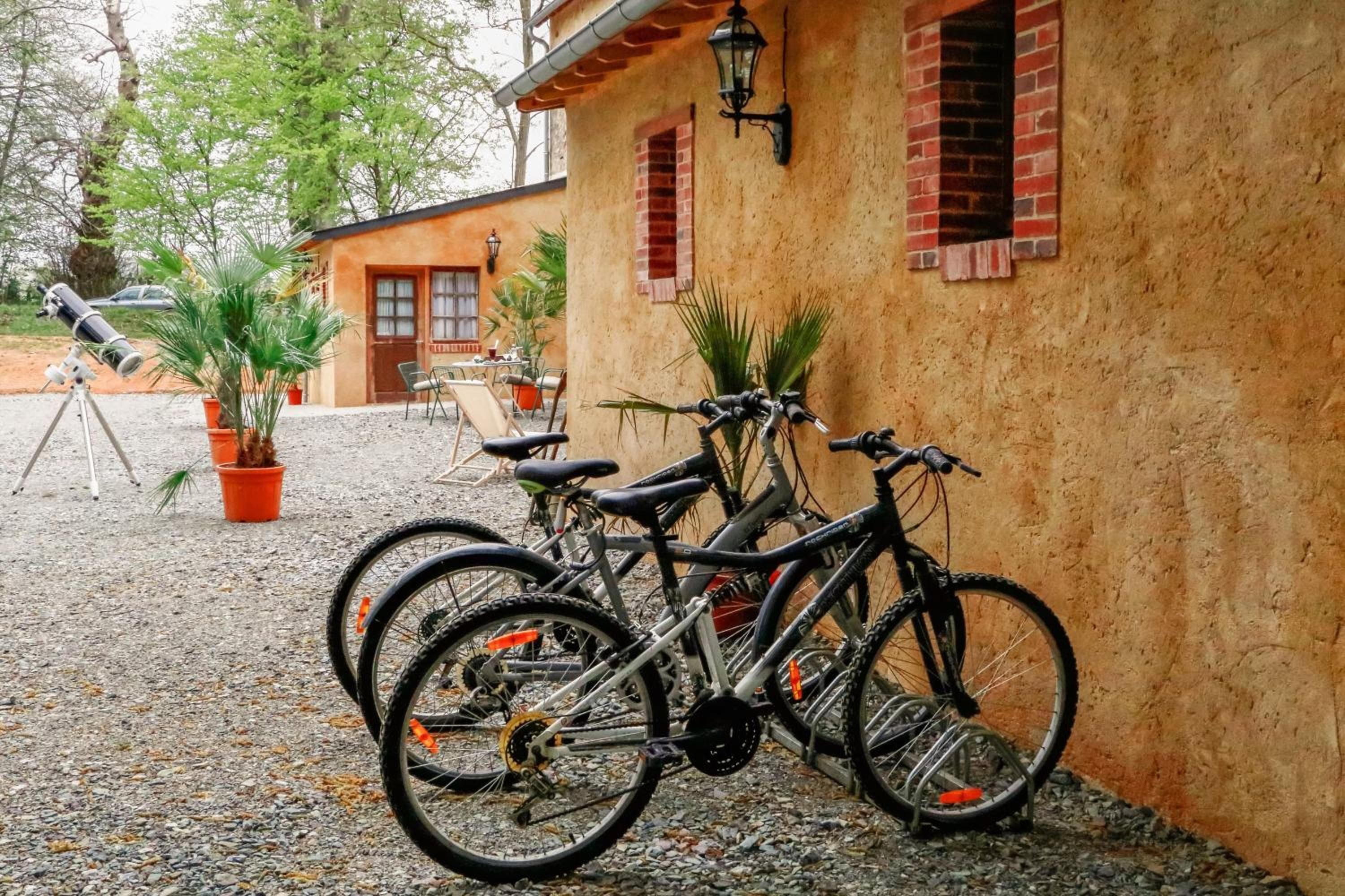Un edificio con fachada rústica, camino de grava y bicicletas apoyadas en la pared.