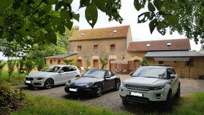 Trois voitures sont garées devant un immeuble à la façade en briques et au toit recouvert de tuiles.