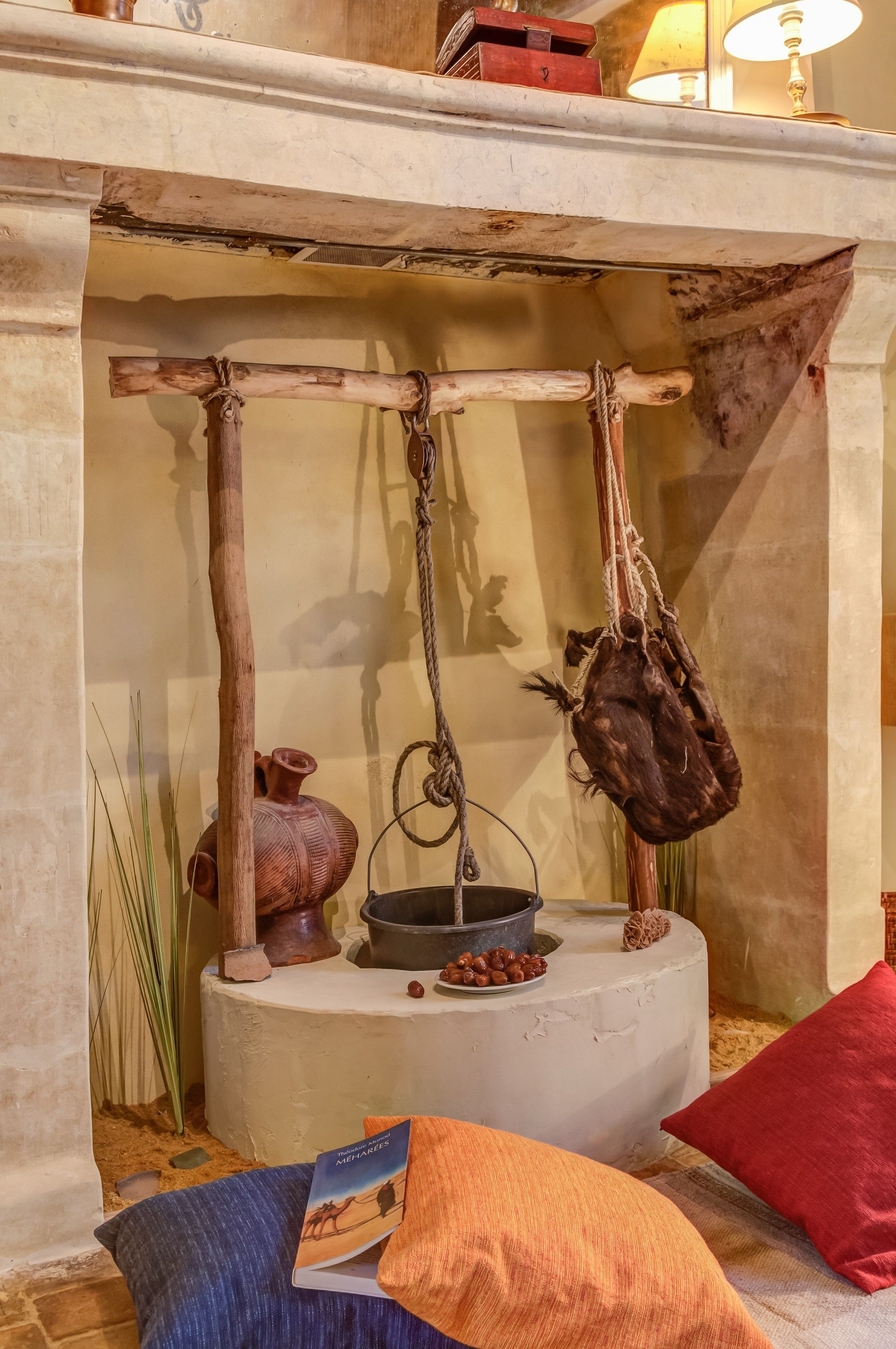 A rustic interior with a wooden shelf holding a pot, a hanging bag, and a book.