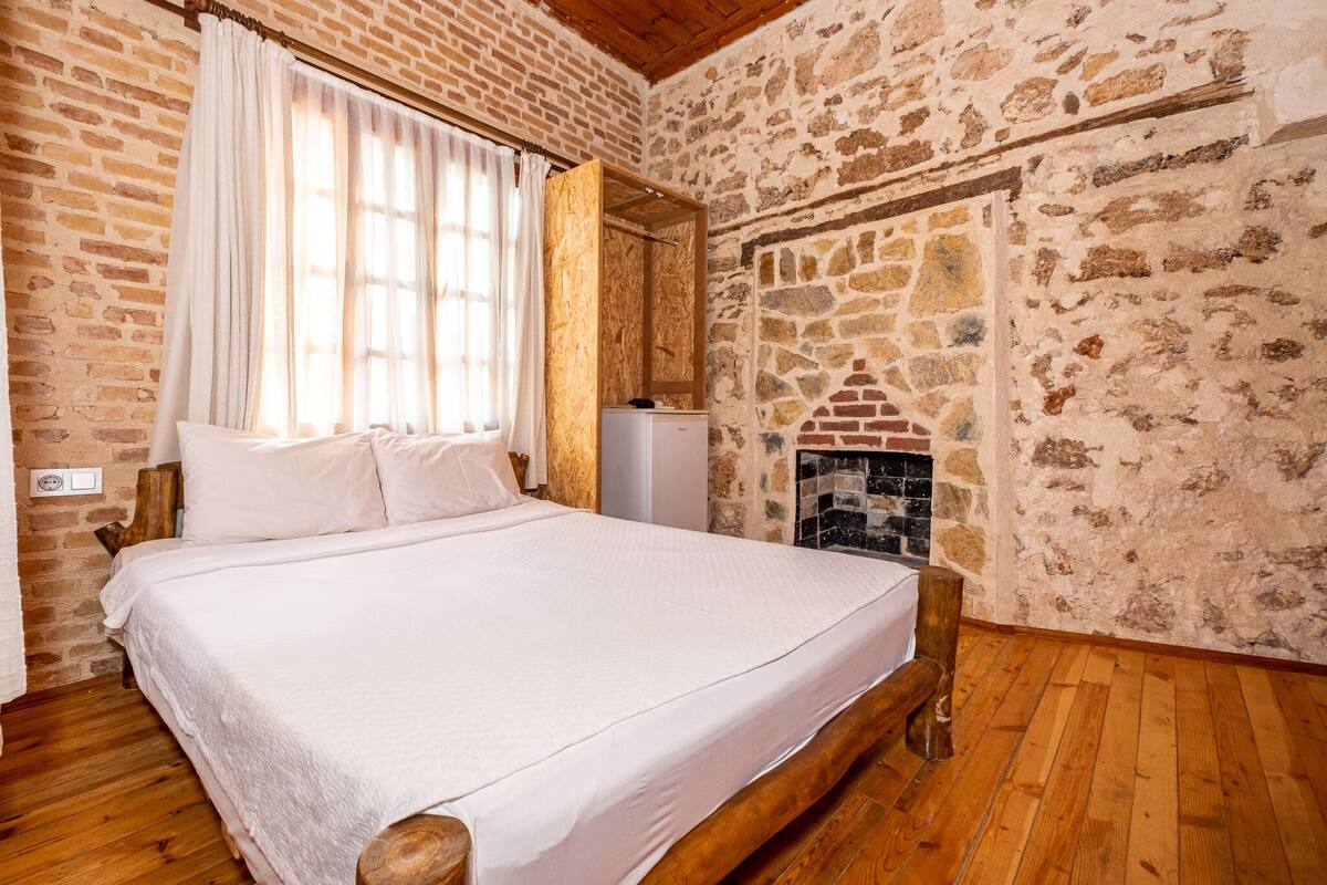 A bedroom with a wooden bed, white bedding, a stone wall, and a fireplace.