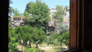 Vista a través de una ventana que muestra un muro de piedra, árboles y un edificio al fondo.