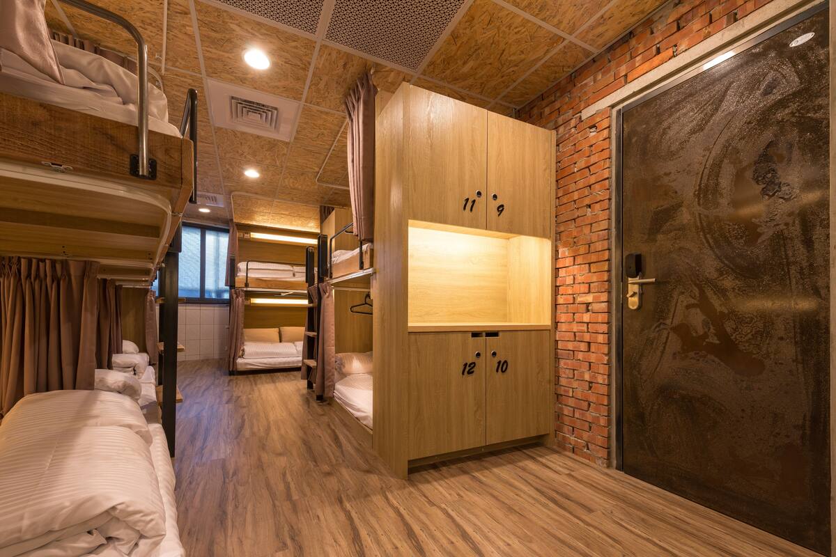A room with bunk beds, a wooden wardrobe with numbers, and a large metal door.