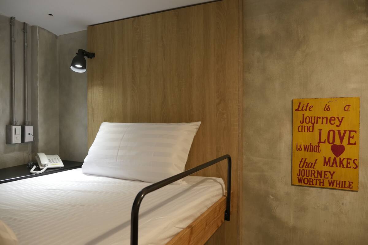 A single bed with a wooden headboard, a bedside lamp, a phone, and a motivational quote on the wall.
