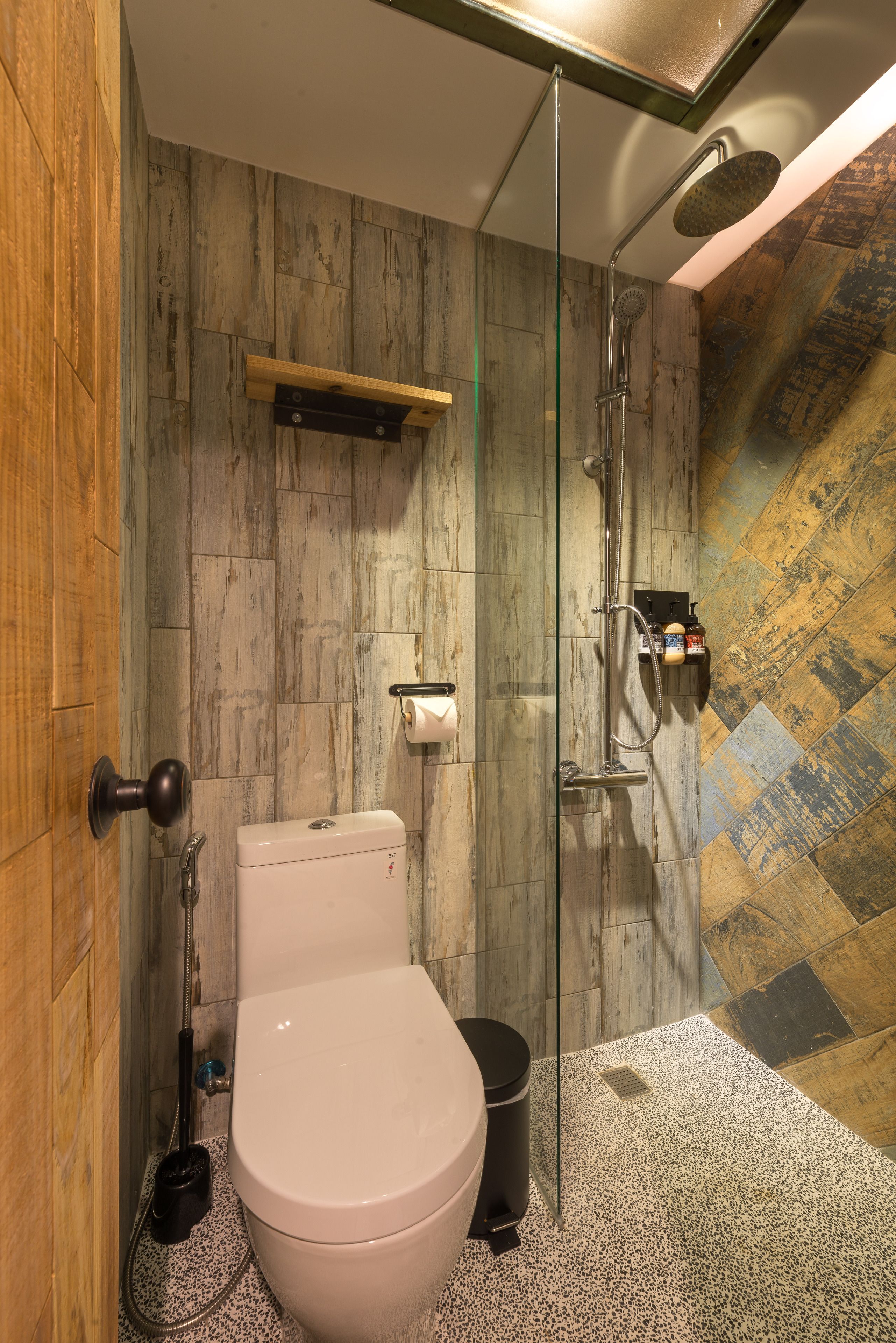 Un baño con inodoro, cabina de ducha de vidrio y pared de madera.