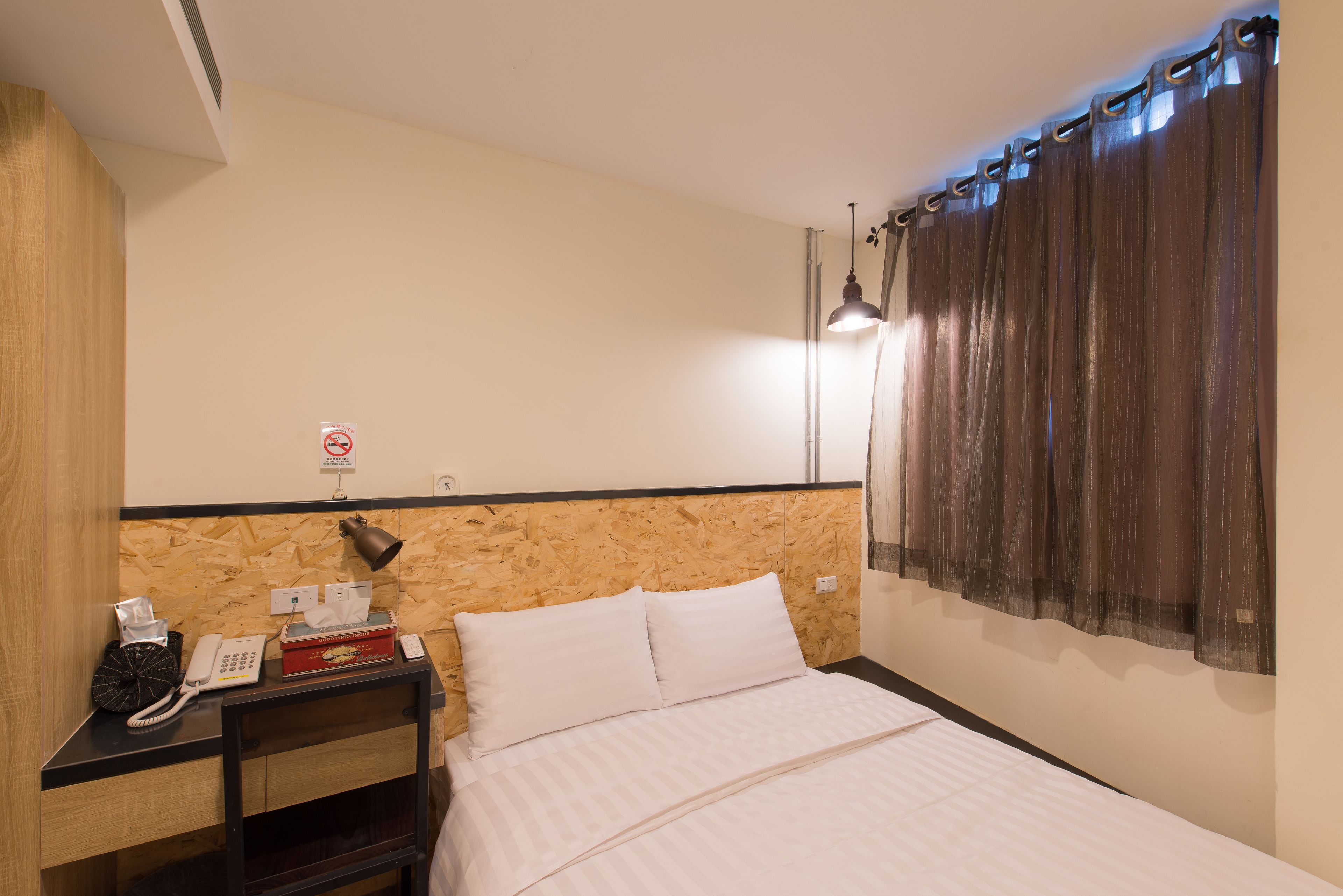 A hotel room with a wooden headboard, a bedside table with a telephone, tissues, and a box of tissues.