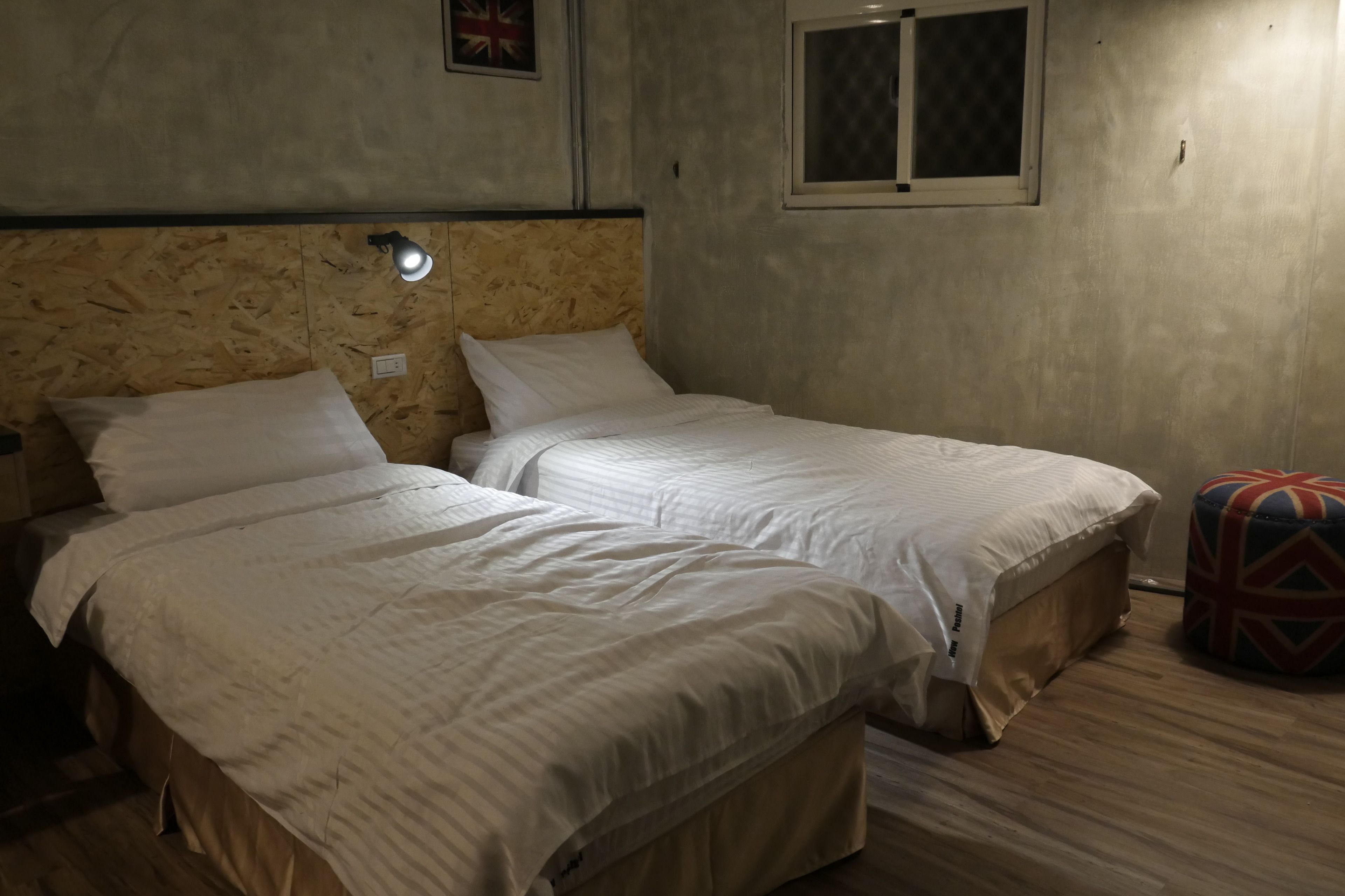 Una habitación con dos camas individuales, una ventana pequeña y una lámpara fijada a la pared.