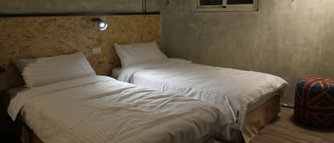 Una habitación con dos camas individuales, una ventana pequeña y una lámpara fijada a la pared.