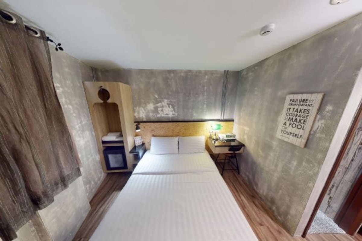A compact hotel room with a bed, a desk, a chair, and a motivational quote on the wall.