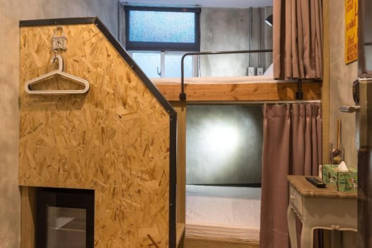 A compact room with bunk beds, a wooden wall, a small window, and a hanging clothes rack.