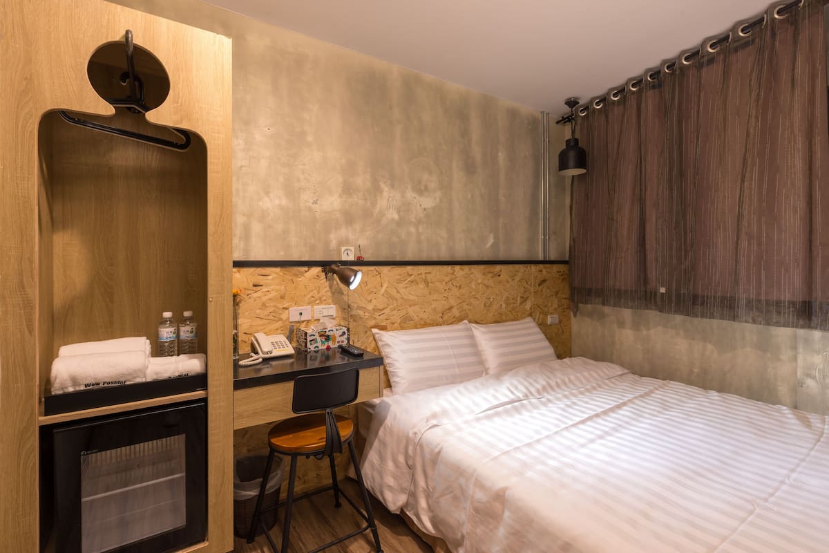 A hotel room with a bed, a desk with a chair, a small TV, and a wardrobe.