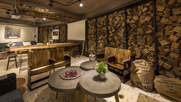 A cozy cafe with wooden furniture, a coffee bar, and a rustic wall with stacked firewood.