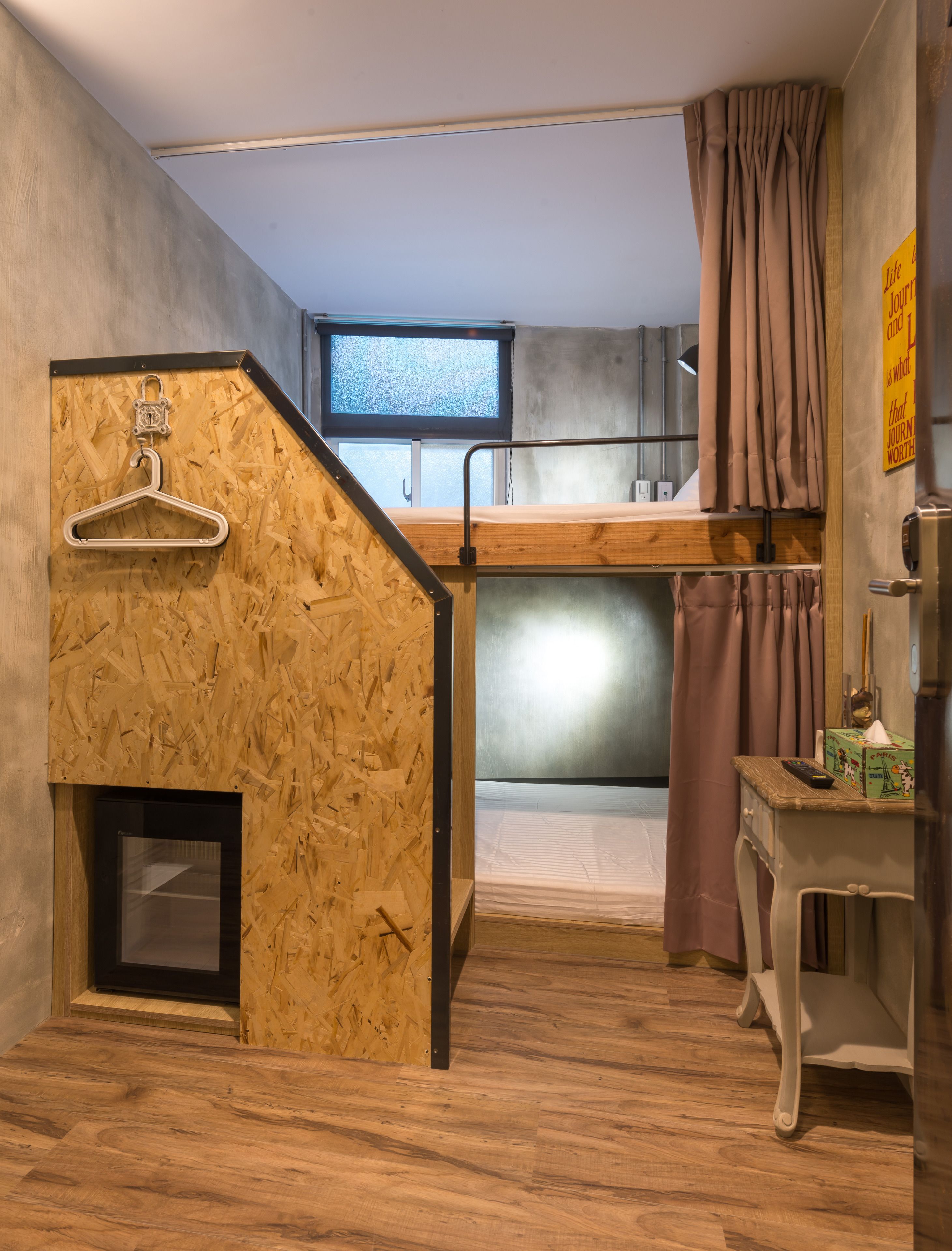 Habitación compacta con literas, una mesita con control remoto y una pared de madera con perchero.
