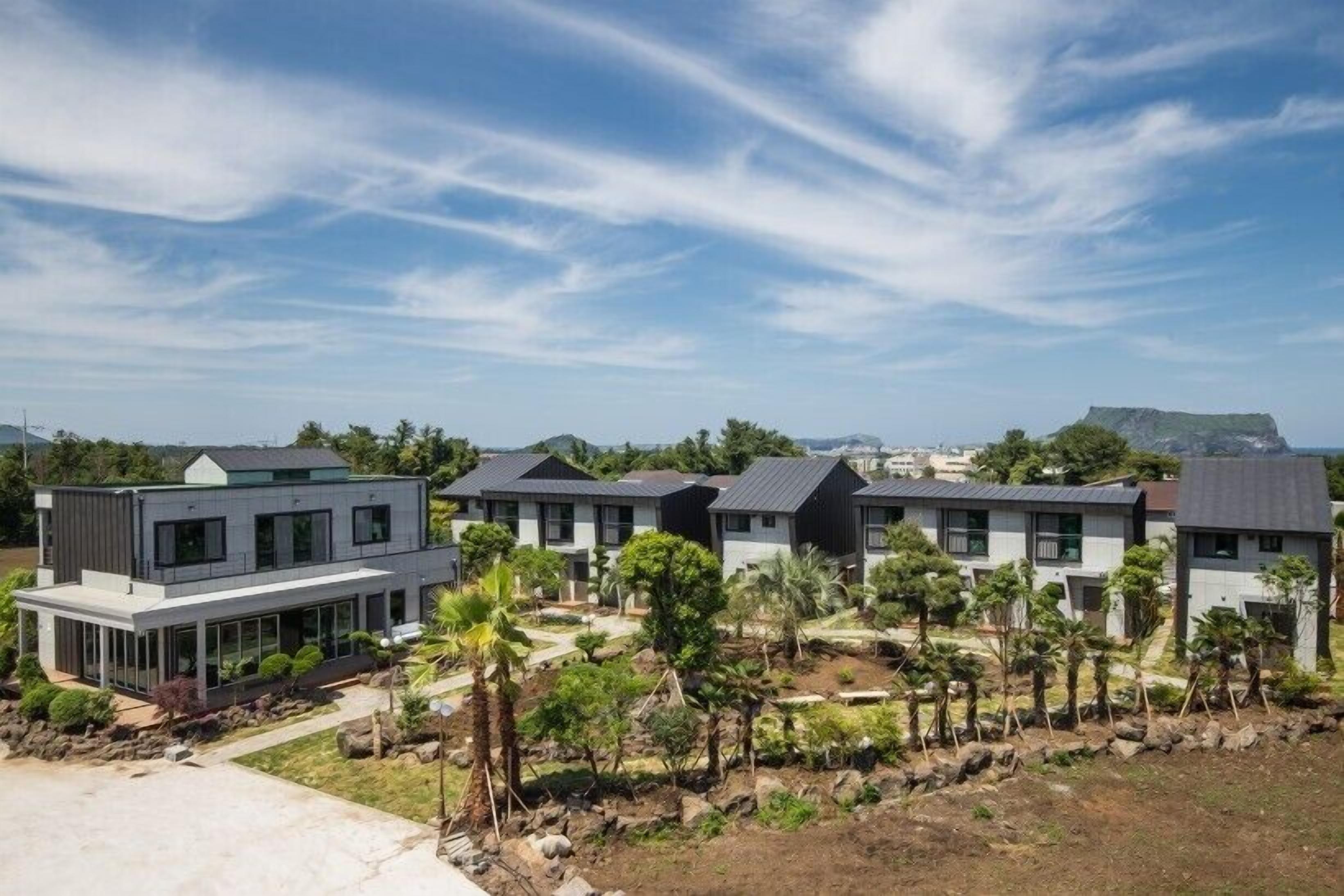 A modern residential complex with multiple two-story houses, featuring large windows and a landscaped garden with palm trees.