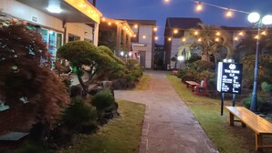 A pathway leading to a building with string lights overhead. There is a signboard with text and a bench on the right. - The Some Pension (Seogwipo)