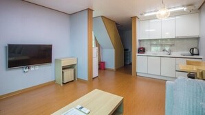 A compact living space with a flat-screen TV, a wooden coffee table, a kitchenette, and a staircase leading to an upper level. - The Some Pension (Seogwipo)
