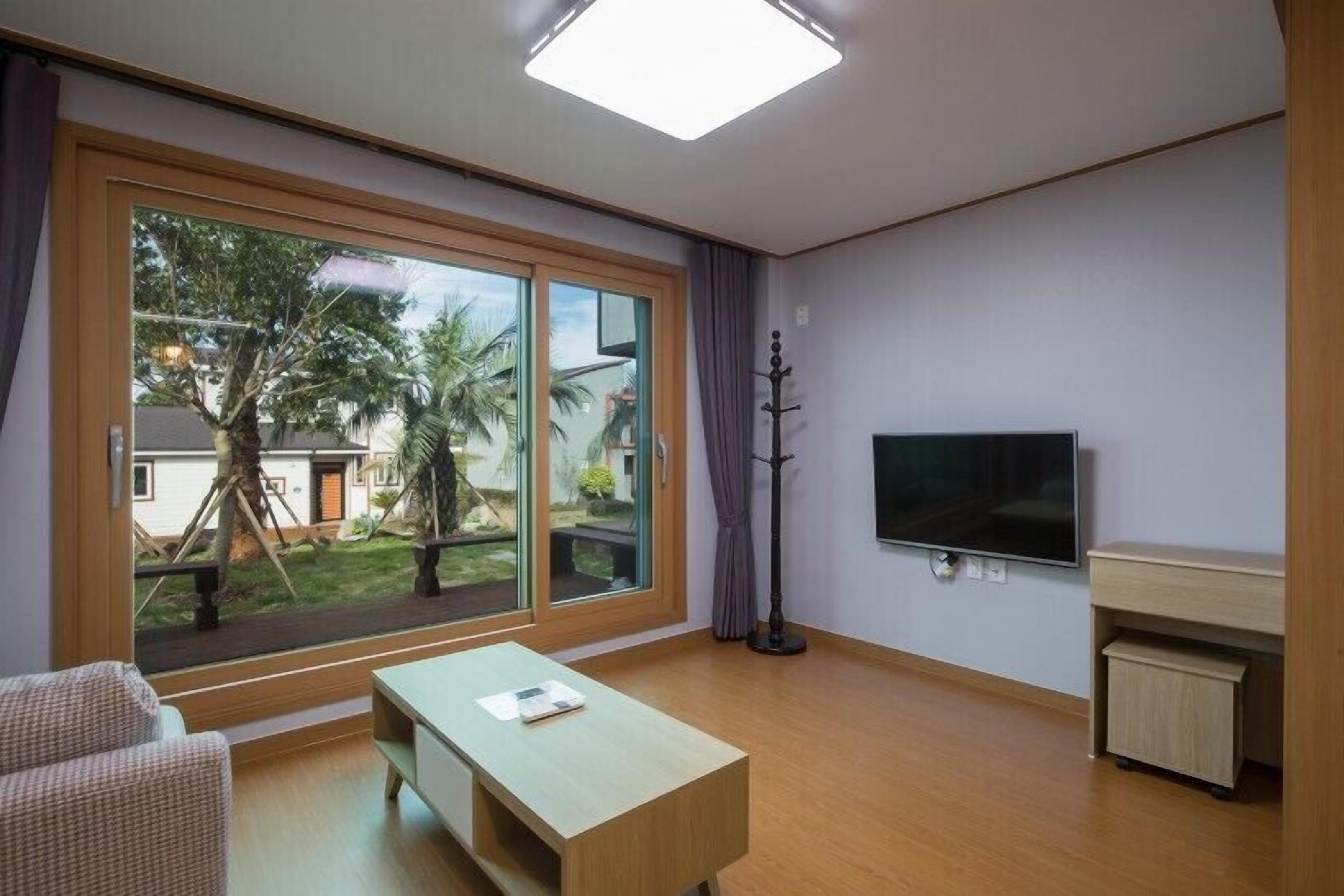 Una sala de estar moderna con un amplio ventanal corredero, un televisor de pantalla plana, una mesa de centro de madera y un escritorio pequeño.