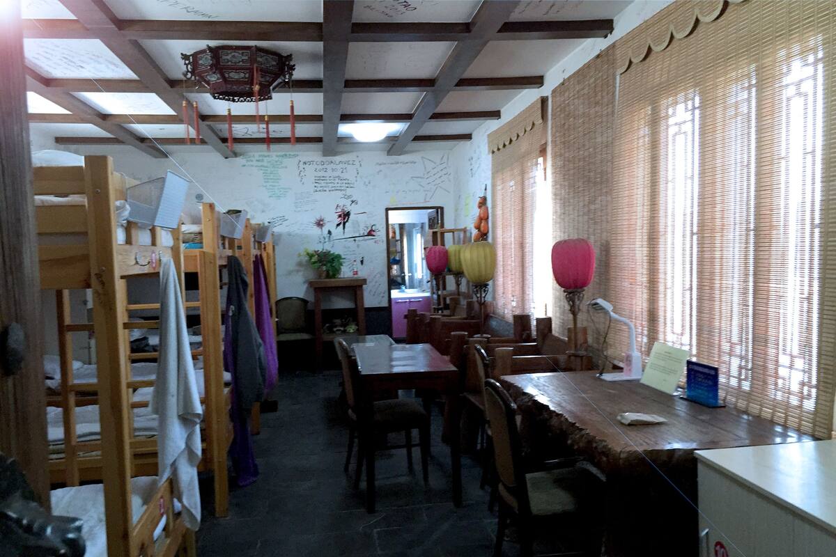 Una habitación con literas, una mesa de comedor, sillas, un refrigerador y una ventana con persianas.