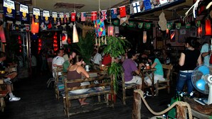 A crowded bar with wooden furniture and flags hanging from the ceiling. - 365 inn - Hostel (Beijing)