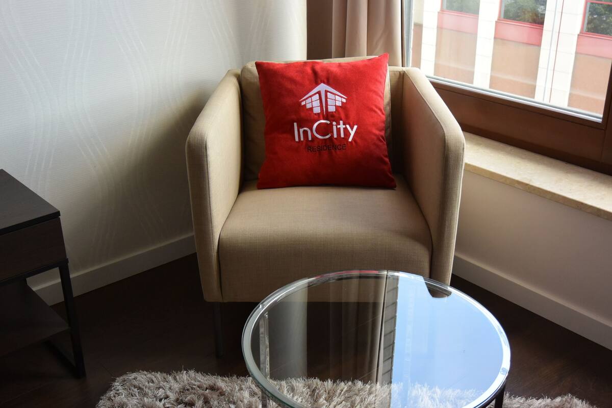 Uma cadeira com travesseiro vermelho identificado como "InCity Residence" e uma mesa de vidro à frente.
