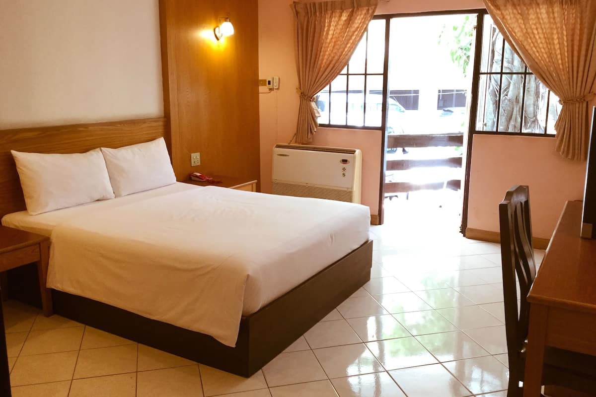 A hotel room with a large bed, a bedside table, a heater, and a window with curtains.