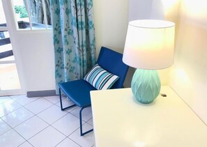 A room with a blue chair, a striped pillow, and a white lamp on a white table. - Pattaya at Nine (Pattaya)