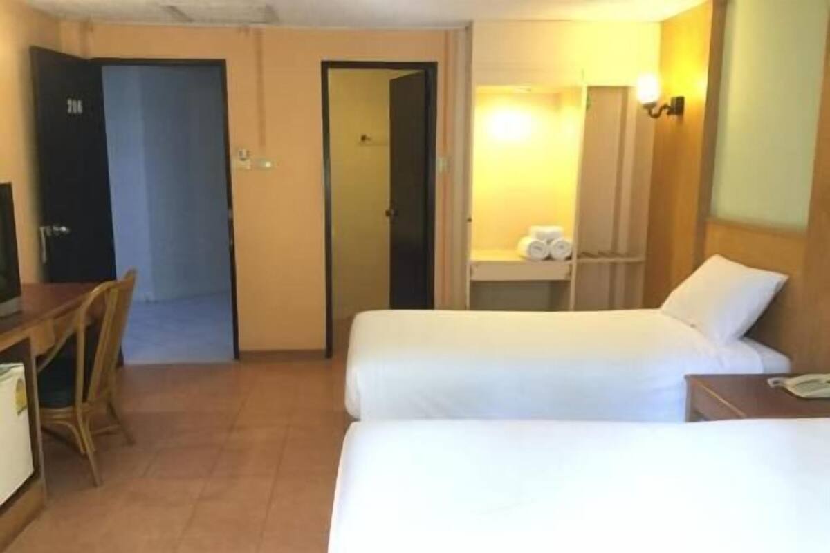 A hotel room with two beds, a desk, a chair, a small table, a mirror, and a bathroom visible through an open door.