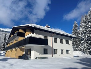 Un edificio moderno con techo inclinado, ventanas grandes y un paisaje cubierto de nieve.