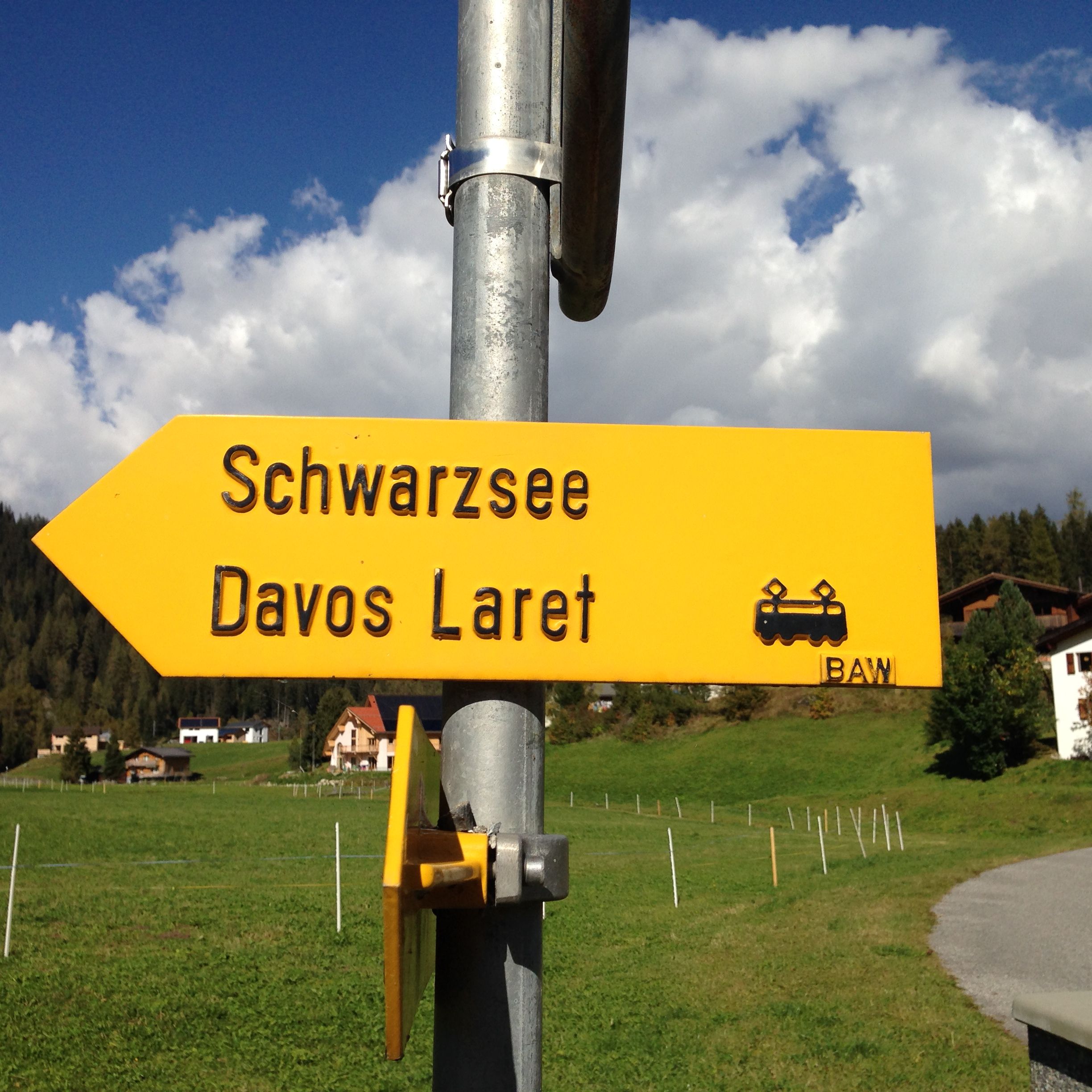 Un cartel direccional con la inscripción 'Schwarzsee Davos Laret' y un símbolo de tren, montado sobre un poste metálico.