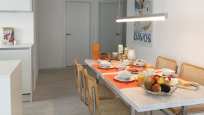 Een moderne eetruimte met een lange tafel gedekt voor het ontbijt, met diverse soorten eten en een fruitschaal.