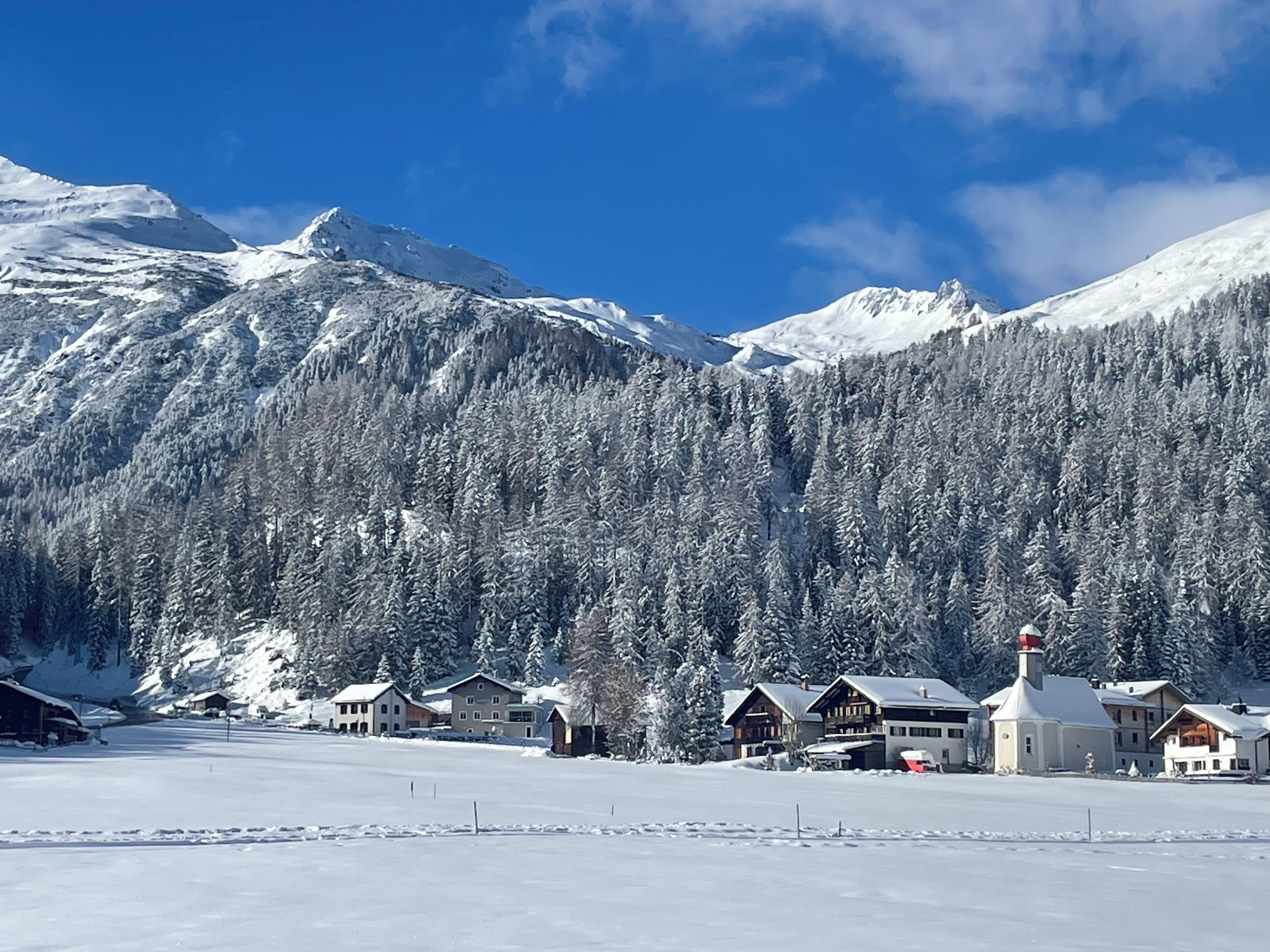A snow-covered mountain landscape with a row of wooden cabins and a church in the foreground.