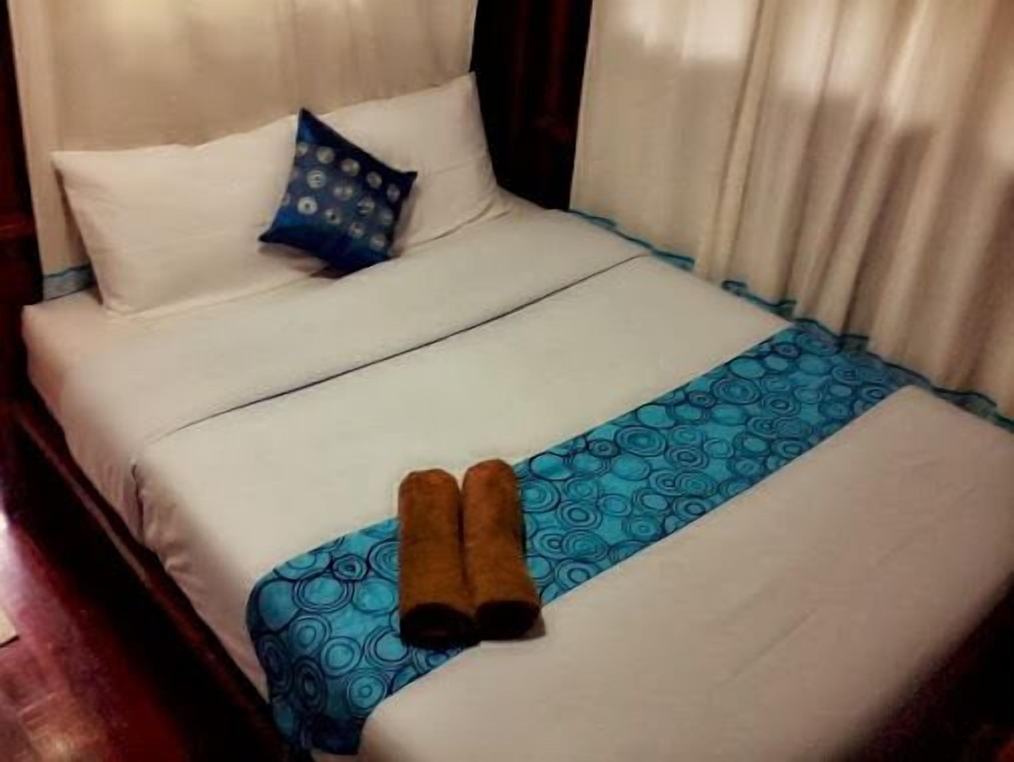 Een net opgemaakt bed met witte lakens, een blauw beddegoed met patroon en twee bruine handdoeken.