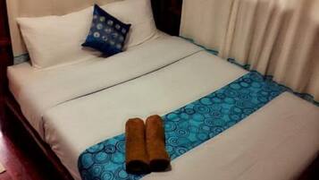 Een net opgemaakt bed met witte lakens, een blauw beddegoed met patroon en twee bruine handdoeken.