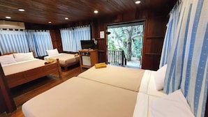 Een kamer met twee bedden, een televisie en een balkon met uitzicht op bomen.