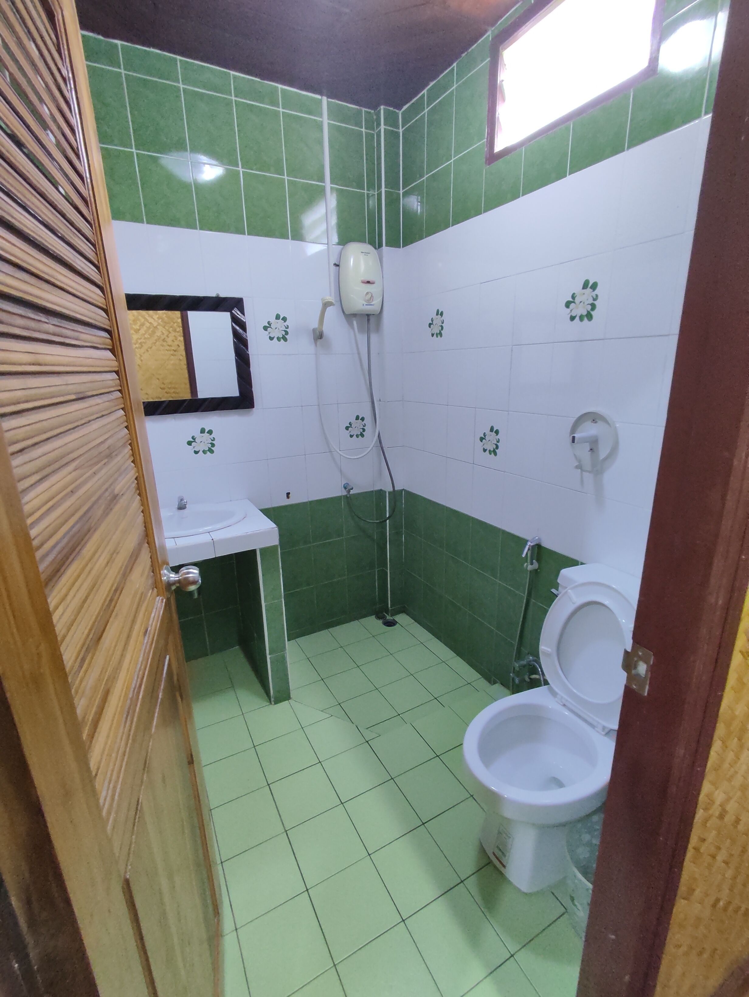 A small bathroom with green and white tiles, a sink, a toilet, and a shower.
