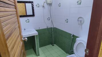 A small bathroom with green and white tiles, a sink, a toilet, and a shower.