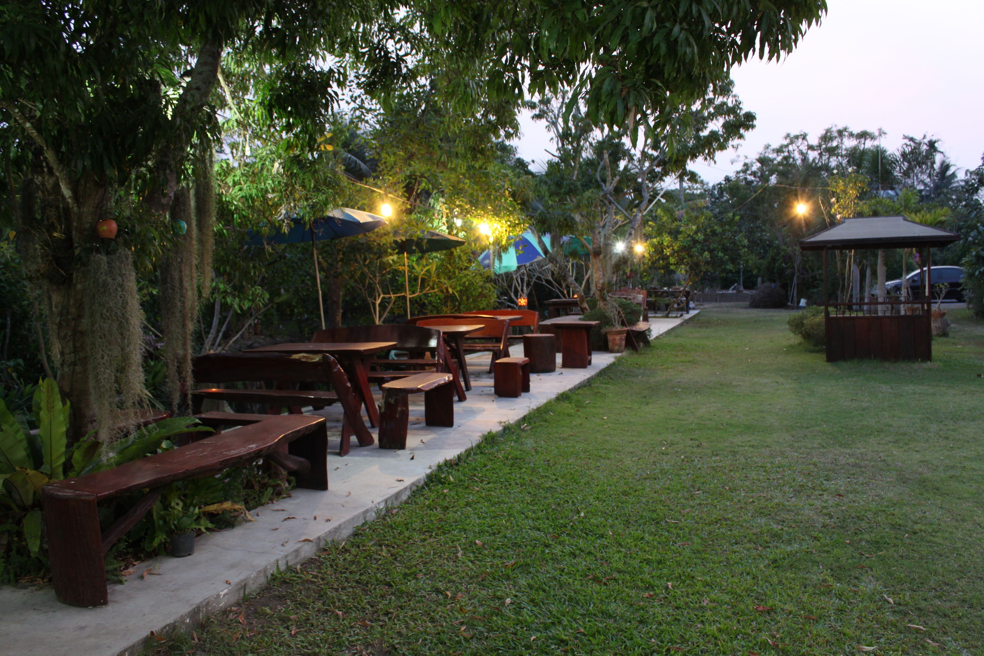 An outdoor patio with wooden benches and tables, surrounded by trees and a gazebo.