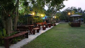 An outdoor patio with wooden benches and tables, surrounded by trees and a gazebo.