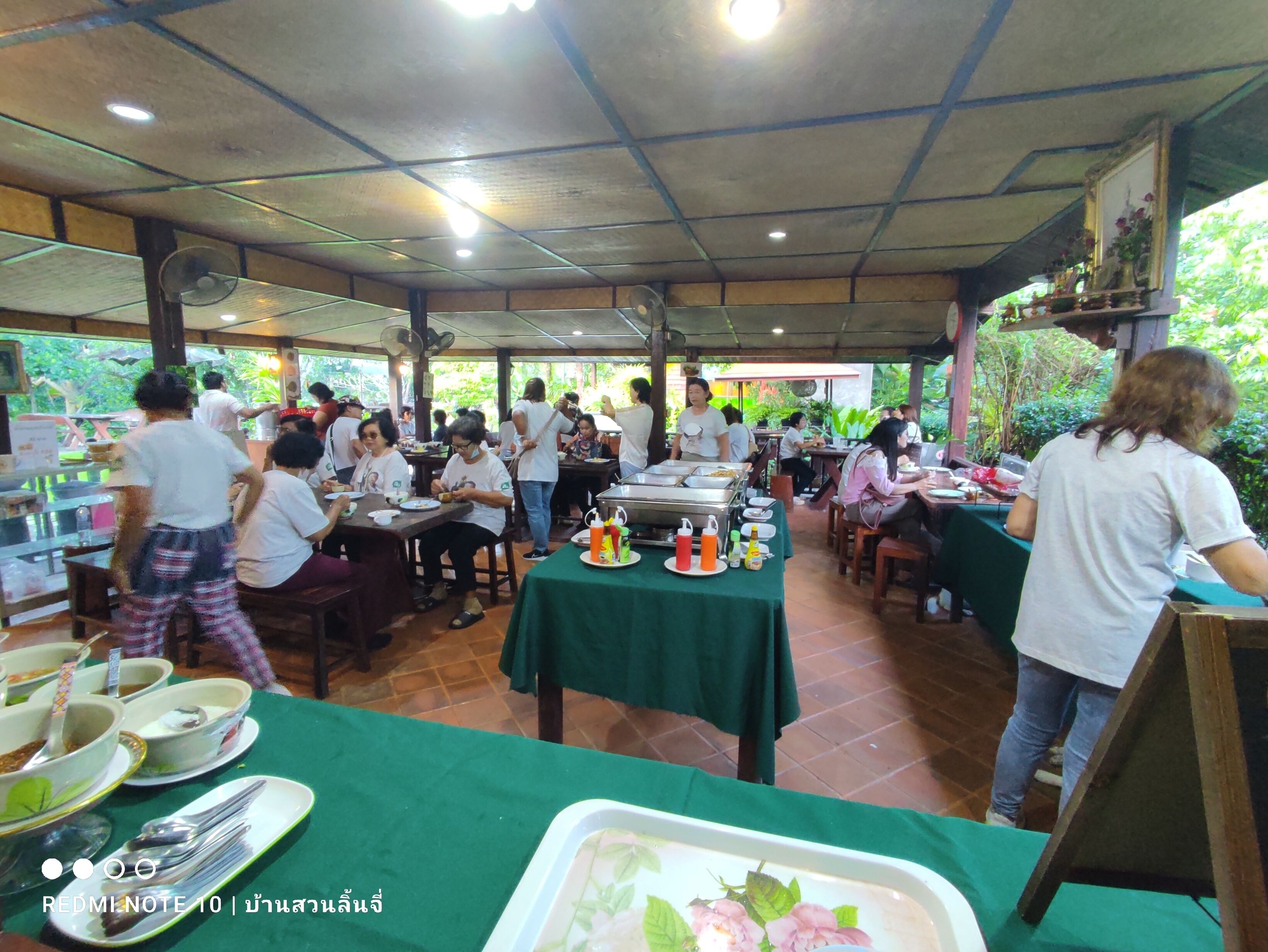 A communal dining area with tables covered in green tablecloths, serving dishes, and utensils.