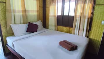 Una cama individual con ropa blanca, un almohilarón marrón y una toalla enrollada. Un equipo de aire acondicionado está montado en la pared sobre la ventana.