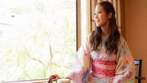 Une personne est assise à une table, une tasse à la main, dans une pièce d’où l’on peut voir des arbres à travers la fenêtre.