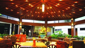 An indoor dining area with wooden tables and chairs, a central flower arrangement, and a ceiling with a radial light fixture. - Batangas Country Club (Batangas City)