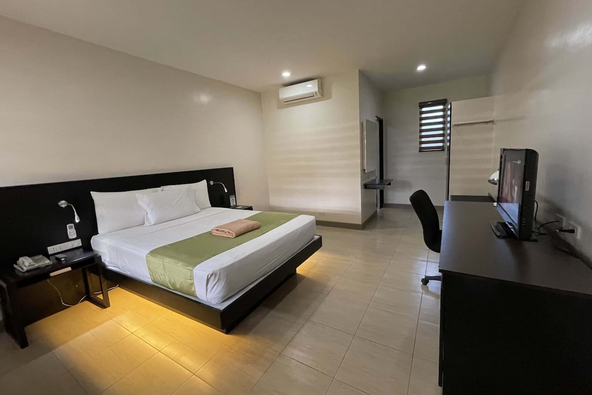 Une chambre d’hôtel comprenant un lit, une table de chevet, une lampe, un bureau, un ordinateur et un espace douche.