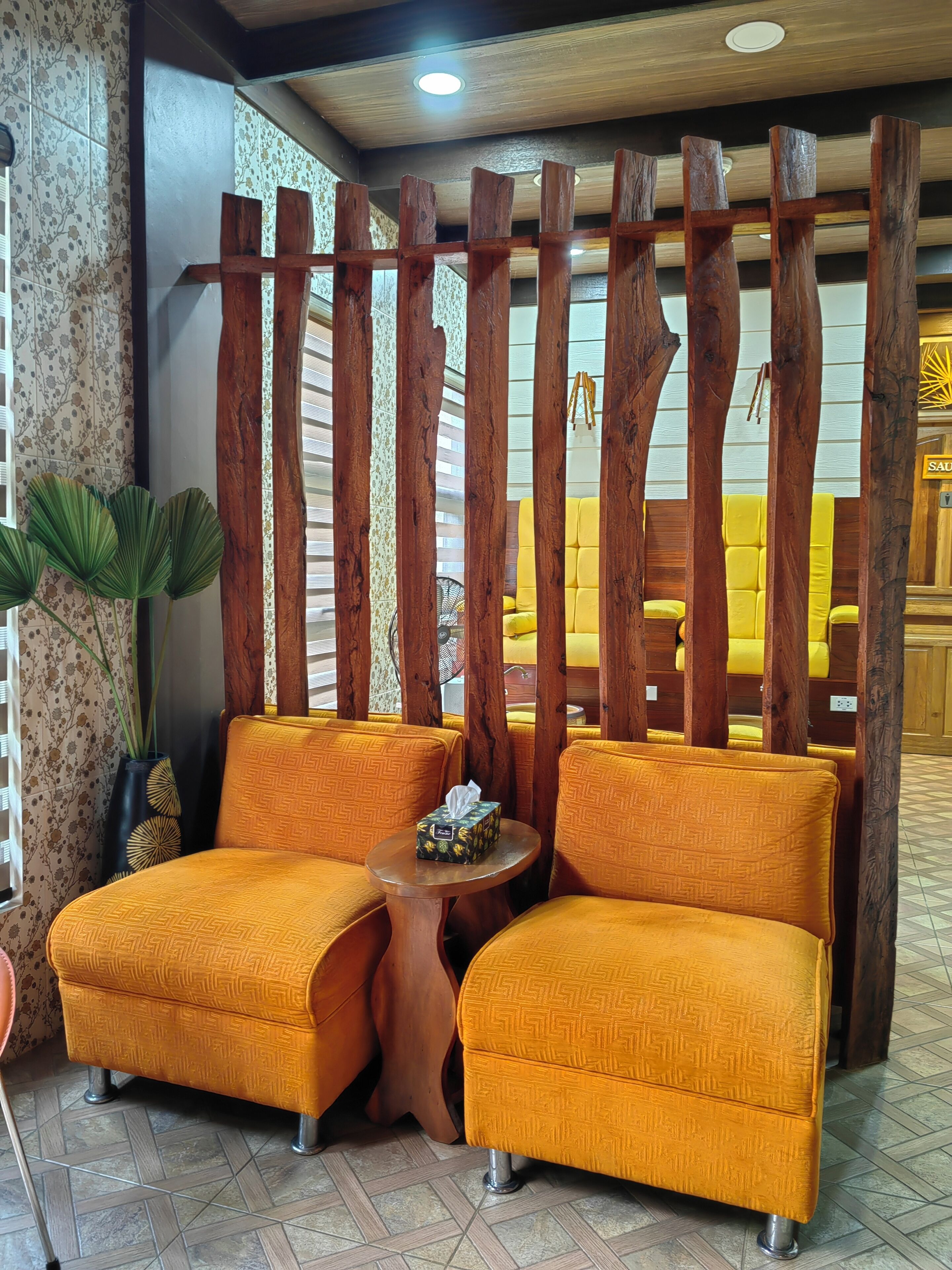 A seating area with two yellow cushioned chairs, a small round table with a tissue box, and a decorative wooden partition.